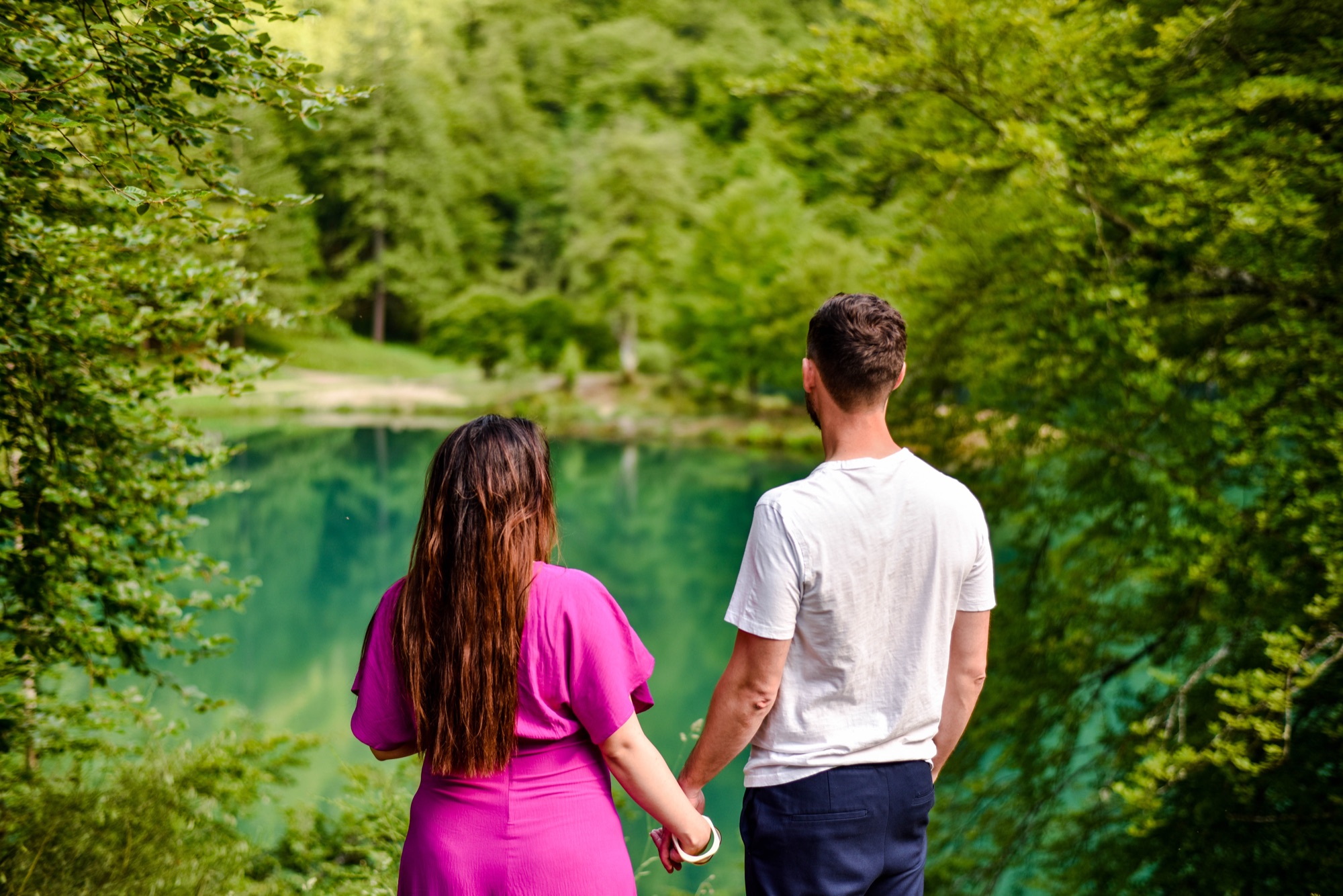 Couple de dos au bord d'un lac turquoise en forêt