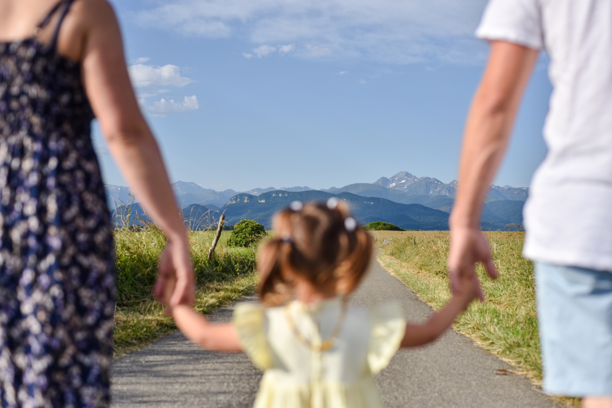 Famille de dos tenant les mains de leur petite fille, avec les Pyrénées en fond